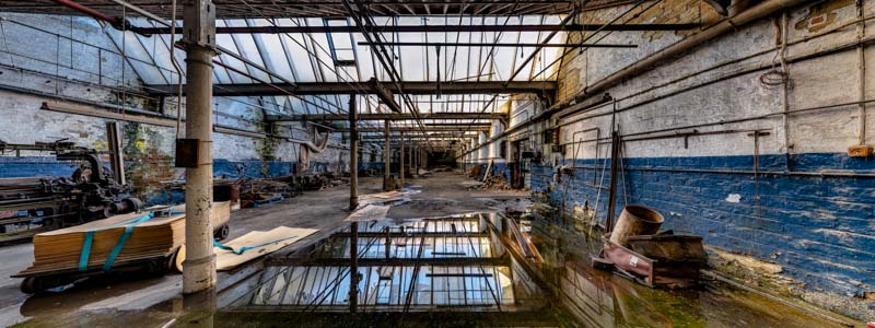 Interior of Sunny Bank Mills weaving shed. Image shows decay, puddles of water and old loom machinery.